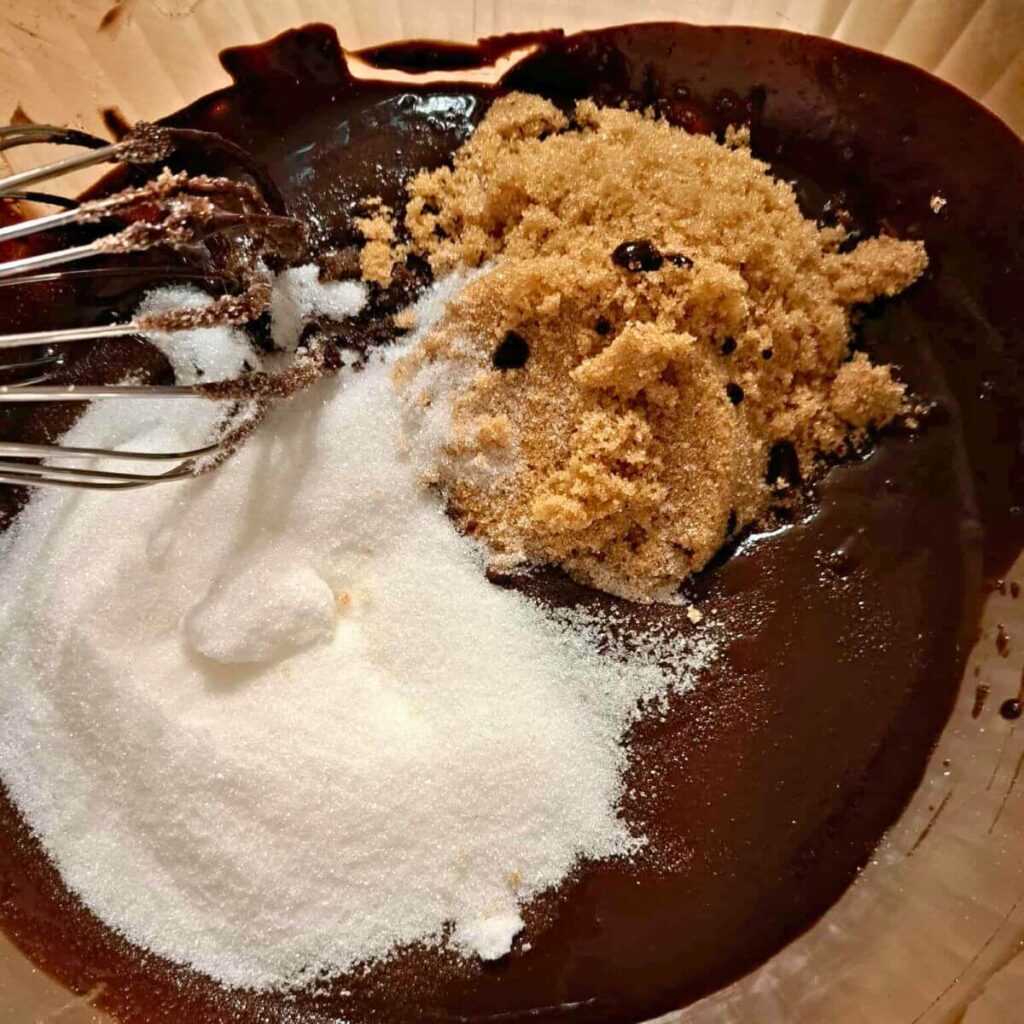 adding sugar and brown sugar to butter and cocoa in a mixing bowl