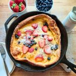 the Best dutch baby made with fresh milled flour in cast iron skillet with strawberries and blueberries