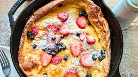 the Best dutch baby made with fresh milled flour in cast iron skillet with strawberries and blueberries